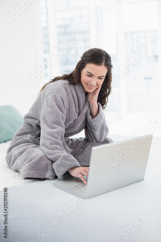 Casual brunette in bathrobe using laptop in bed