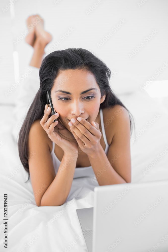 Astonished natural woman phoning while using her notebook Astonished natural woman phoning while using her notebook