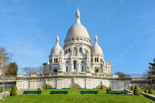 Canvas Print Front view of the bright white basilica of the Sacred Heart of Paris, situated at the top of the Montmartre hill, seen from the Louise Michel park by a sunny spring morning