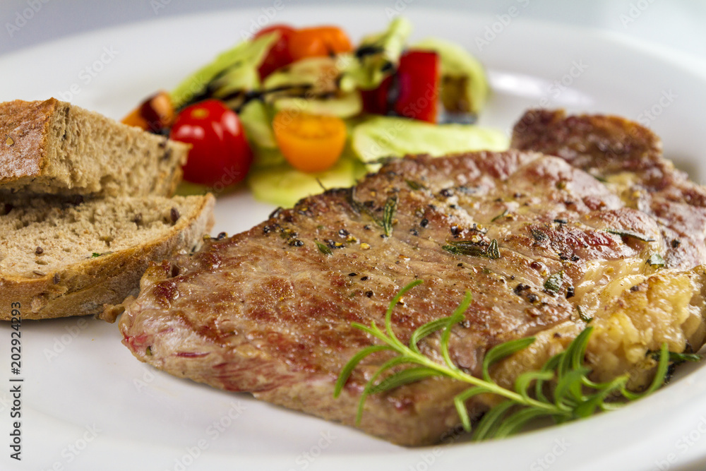 Ripened seasoned beef rump or striploin steak cooked on white plate with salad and home made bread Ripened seasoned beef rump or striploin steak cooked on white plate with salad and home made bread