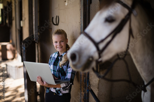 Bilde på lerret Teenage girl using laptop in the stable