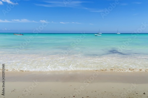 a beach in Punta Cana, in the background of a boat and a yacht, against a background of clouds and a blue sky, the Atlantic Ocean, the Dominican Republic