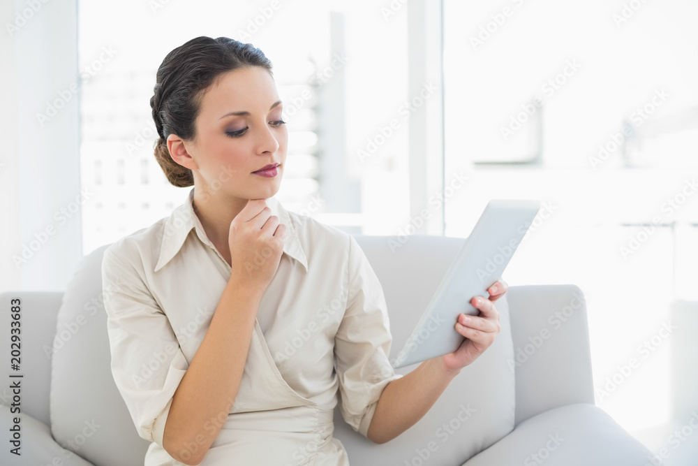 Thoughtful stylish brunette businesswoman looking at a tablet pc Thoughtful stylish brunette businesswoman looking at a tablet pc