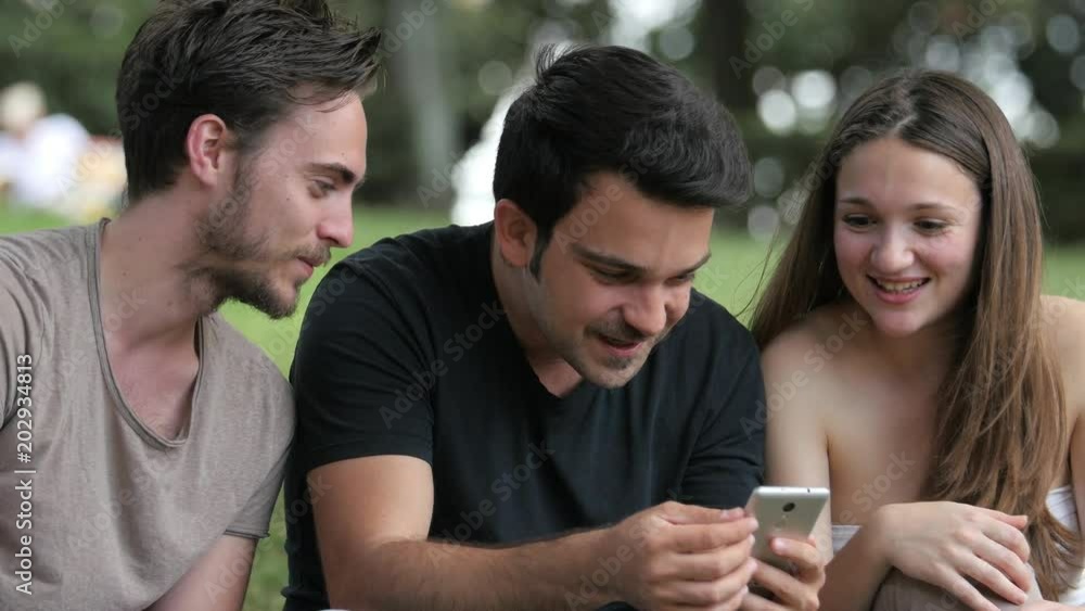 group of friends at the park laughing looking at the smartphone group of friends at the park laughing looking at the smartphone