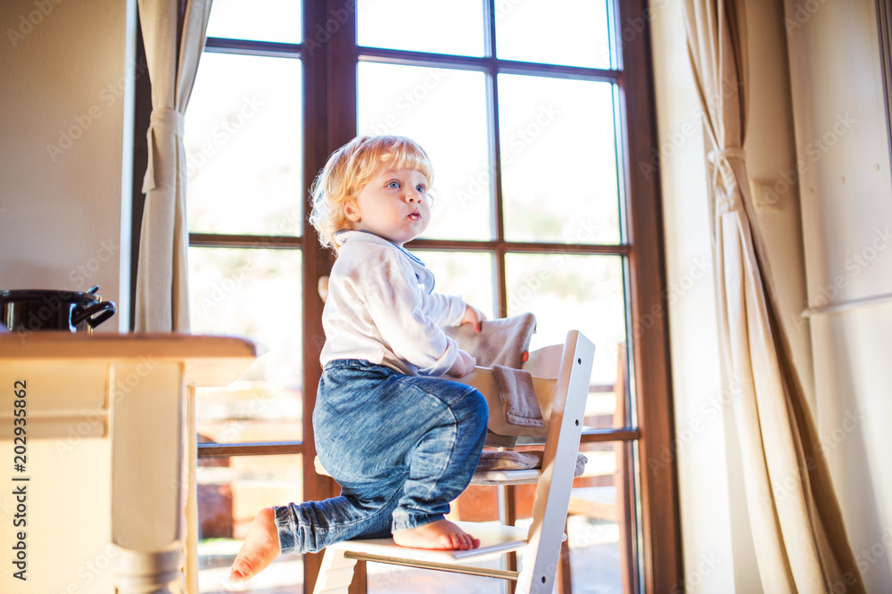 Toddler boy in a dangerous at home, climbing into highchair. Toddler boy in a dangerous at home, climbing into highchair.