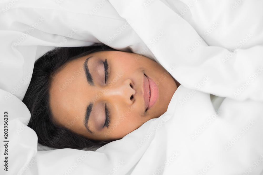Lovely smiling woman lying on bed under cover 