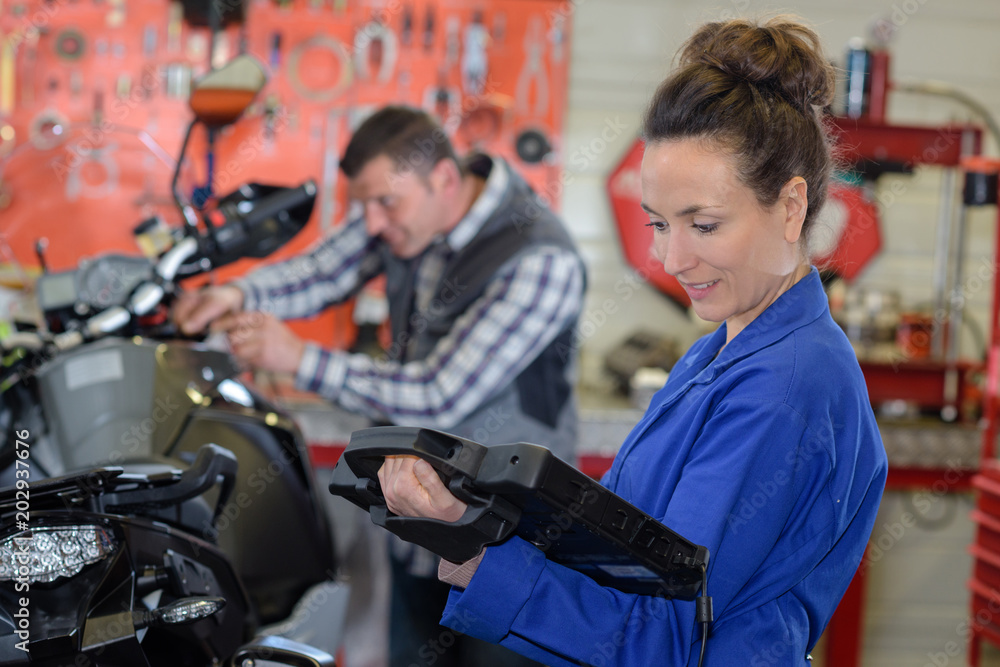 Woman holding computerised device in motorcycle garage Woman holding computerised device in motorcycle garage