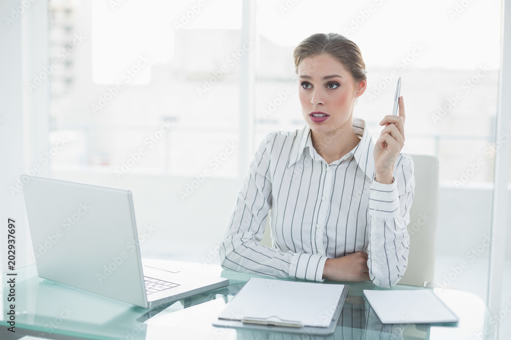 Beautiful thinking businesswoman holding a pen sitting at her desk Beautiful thinking businesswoman holding a pen sitting at her desk