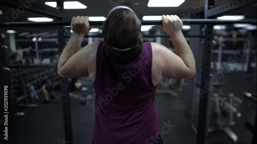 Man trying to pull up his heavy body, increase muscle strength, workout in gym photo