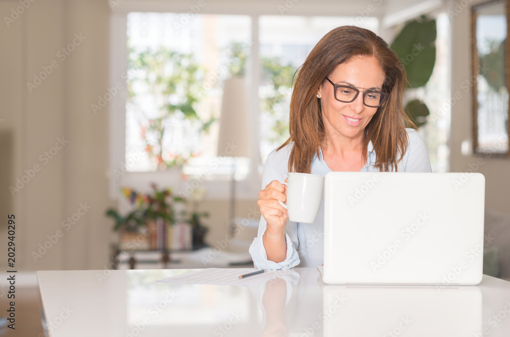 Middle age woman using computer and drinking coffee, indoor Middle age woman using computer and drinking coffee, indoor