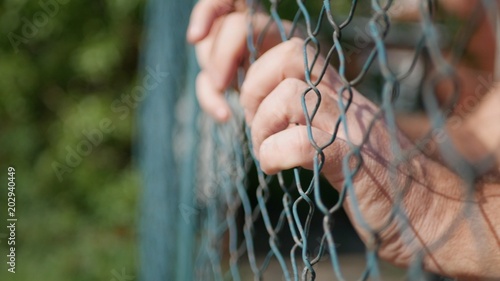 Man Hands Hanging in a Metallic Fence