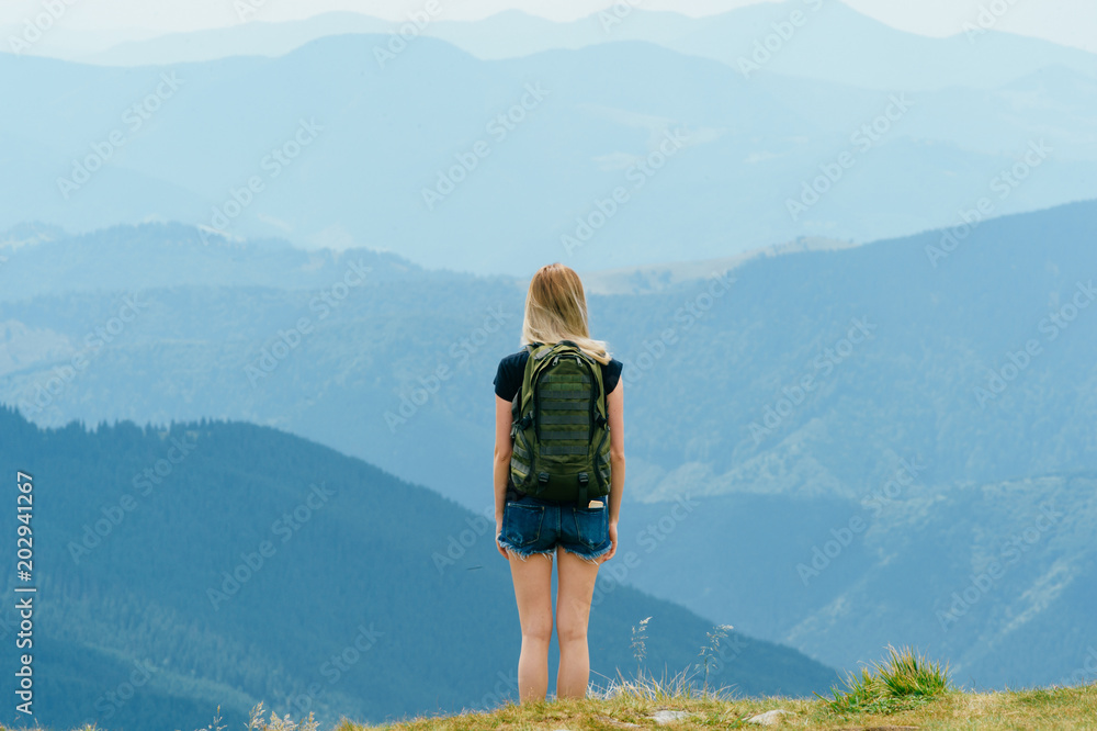 Young girl relaxing and enjoying scenic view on top of mountain.  Bliss and happiness. Beautiful summer nature landscape. Lonely young blonde teen traveler dreaming outdoor on vacation.  Romantic mood