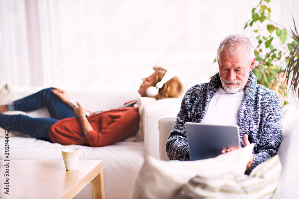 Senior couple with tablet and headphones relaxing at home. Senior couple with tablet and headphones relaxing at home.