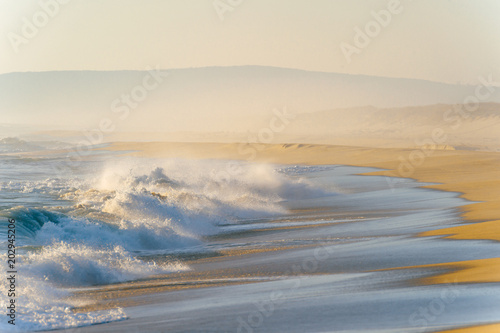 Mediterranean cost ar sunset. Tropical island shore with strong stormy waves in motion. Sunlight on yellow sand beyond ocean. Paradise picturesque seascape. Beautiful nature seaside landscape.  Relax.