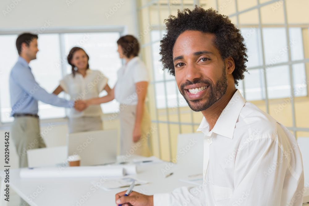 Businessman with colleagues hand shaking in background at office Businessman with colleagues hand shaking in background at office