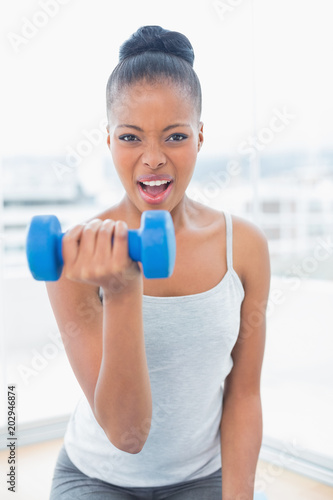 Fit woman working out wit h dumbbell while looking at camera © WavebreakmediaMicro