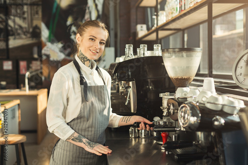 Tattooed barista making coffee in professional coffee machine