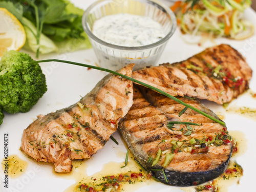 Steaks of salmon, grilled. Served with vegetables and spices on a white plate