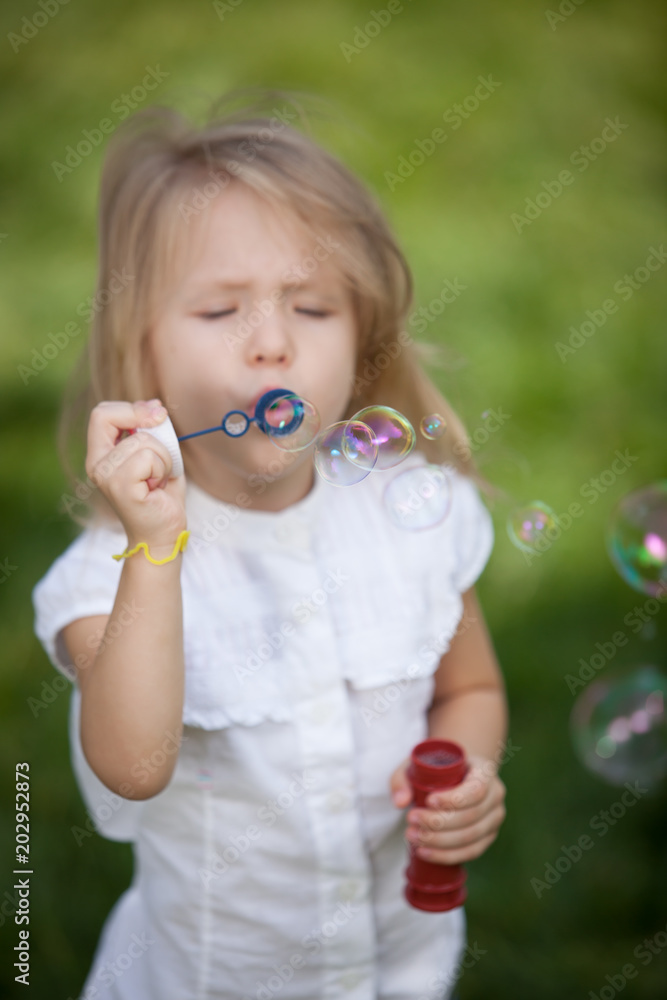 Little girl blowing soap bubbles in summer park, shallow depth of field, focus on bubbles