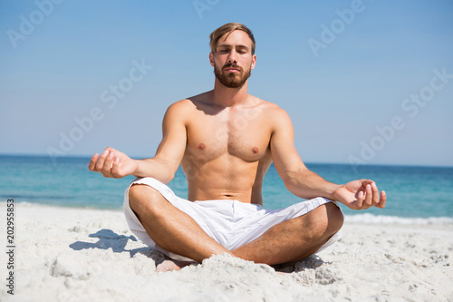 Quadro su tela Full length of shirtless man meditating at beach