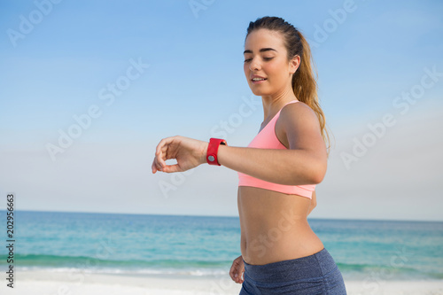 Young woman looking at smart watch while jogging at beach