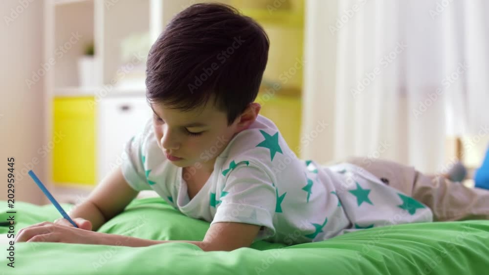 childhood, education, leisure and people concept - happy little boy with notebook and pencils drawing at home childhood, education, leisure and people concept - happy little boy with notebook and pencils drawing at home