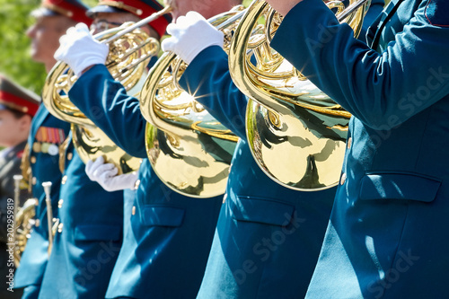 Closeup of military musicians in green uniform and white gloves playing a French horn during a parade in the street. photo