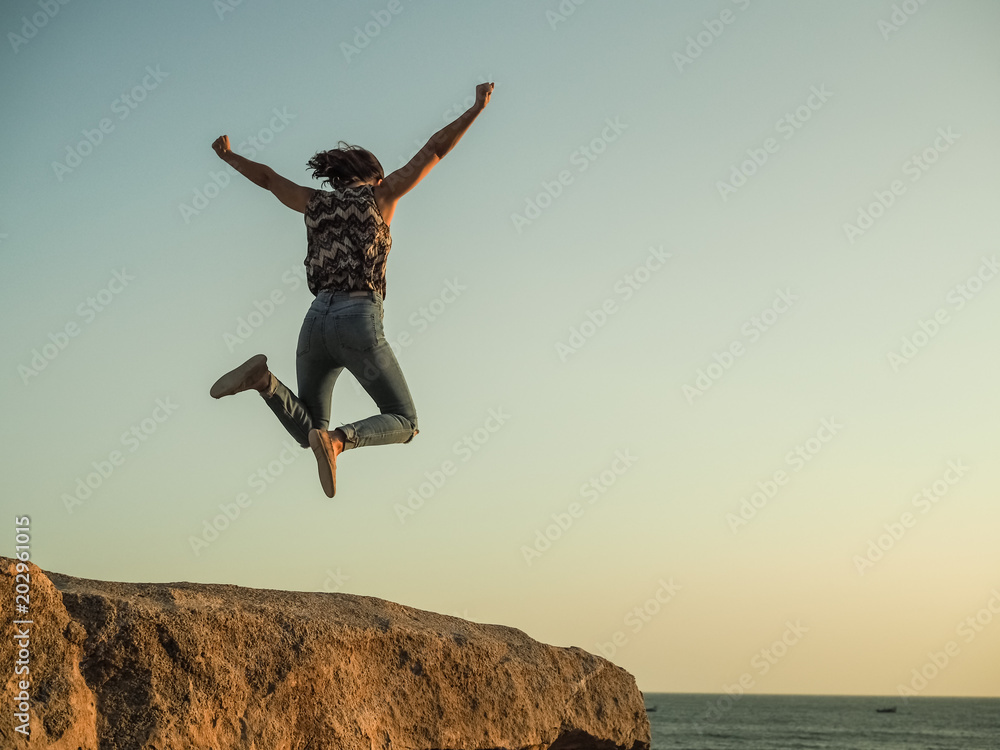 Εκτύπωση καμβά jumping WOMAN celebrates her triumph WITH arms up on top of a rock at the beach
