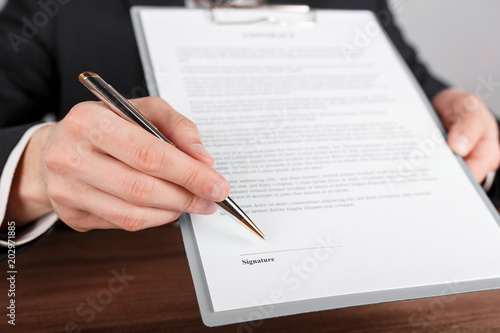Close up of a businessman handing over a contract, attached to a clipboard for signature.