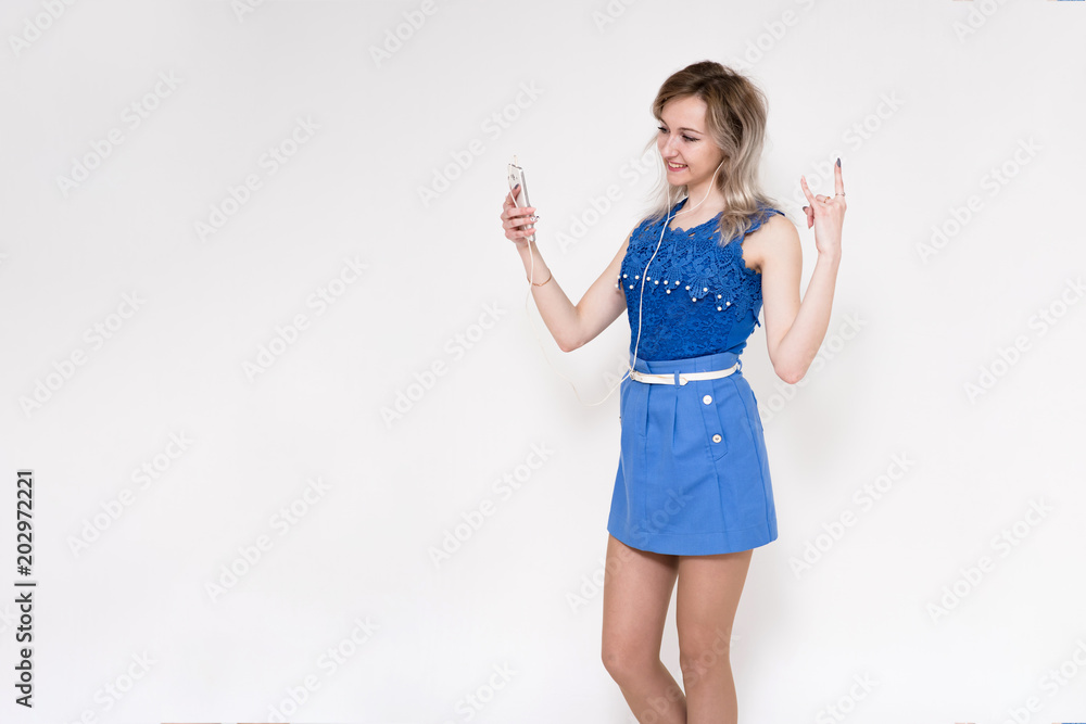 Portrait of a beautiful blonde girl on a white background listening to music in headphones with a smartphone in hands Portrait of a beautiful blonde girl on a white background listening to music in headphones with a smartphone in hands