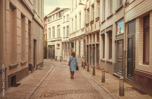 Lonely elegant woman walking on narrow street with old houses and cobbled stones.