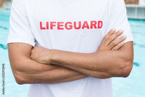 Mid section of lifeguard standing with arms crossed