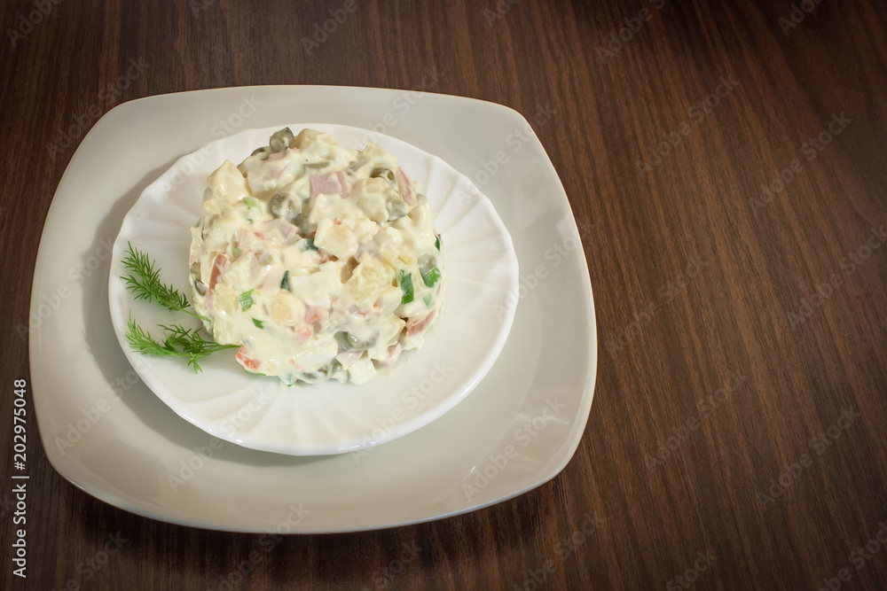 Salad Olivier in a white plate on a brown wooden background. Salad Olivier in a white plate on a brown wooden background.