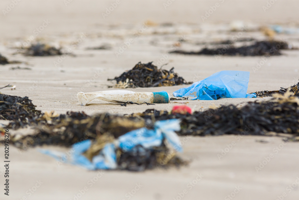 Αυτοκόλλητο Plastic rubbish and bottle washed up on a beach and part buried in the sand an e