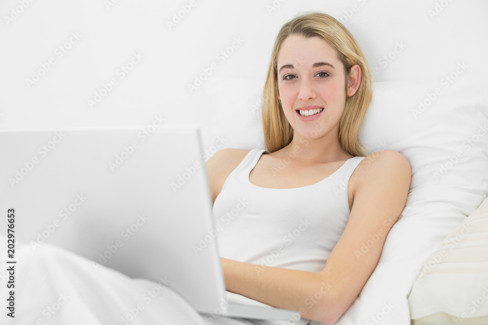 Beautiful young woman lying on her bed using her notebook Beautiful young woman lying on her bed using her notebook