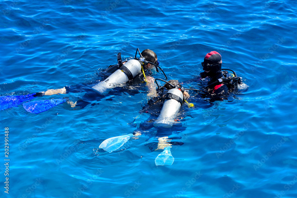 Fototapeta premium Divers on the clear and turquoise Red Sea on immersion in beautiful corals and colorful fish. The teacher teaches the student the rules of immersion in water. Summer, vacation. Egypt