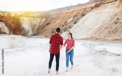 Young woman and man in plaid shirts traveling holding hands at sandy canyon or quarry. Outdoors. Copt space