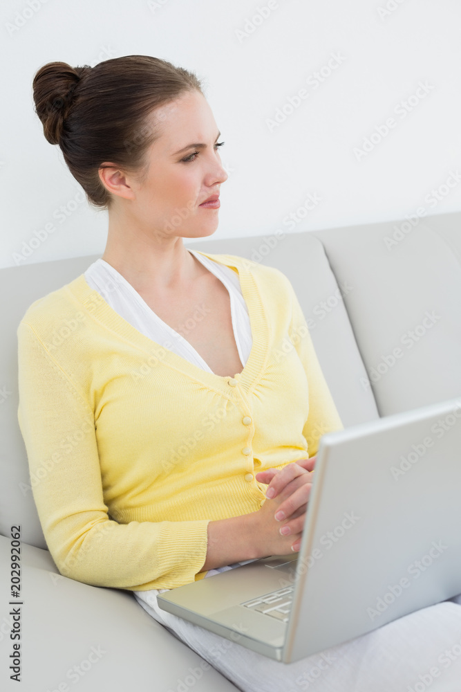Thoughtful casual woman with laptop sitting on sofa Thoughtful casual woman with laptop sitting on sofa