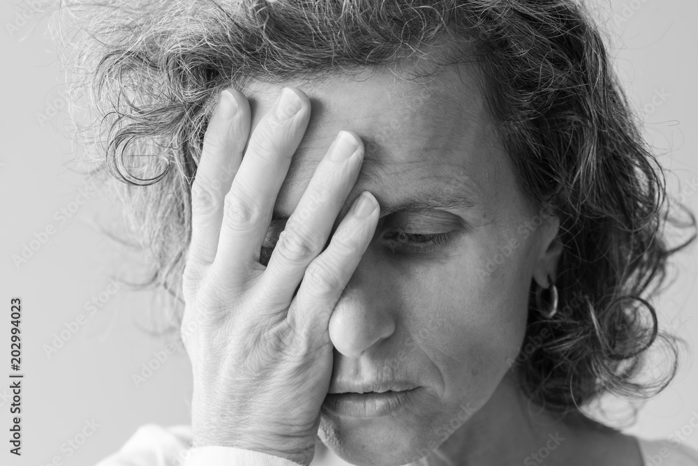 Fototapeta premium Black and white portrait of distressed looking middle aged woman with hand covering face(selective focus)