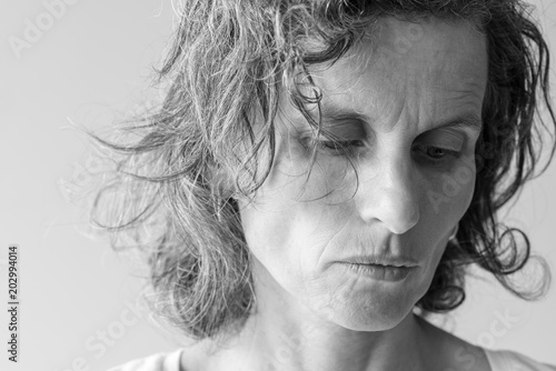 Black and white close up view of distressed looking middle aged woman looking down (selective focus)