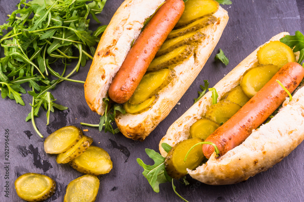 Two hot dogs with cucumber, salad on a dark background - top view Two hot dogs with cucumber, salad on a dark background - top view