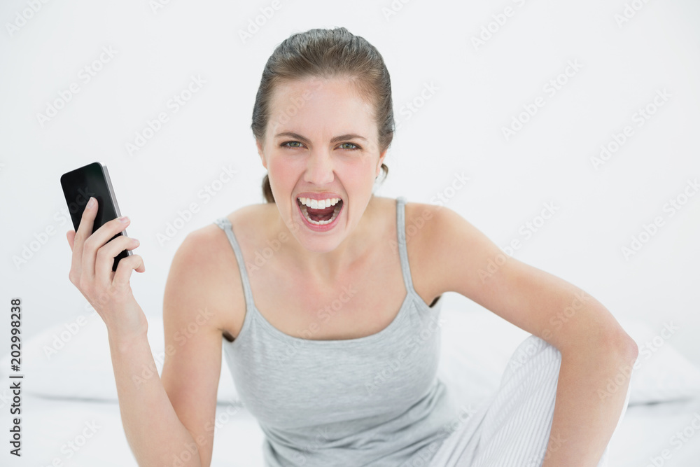 Angry woman shouting with mobile phone in hand on bed Angry woman shouting with mobile phone in hand on bed