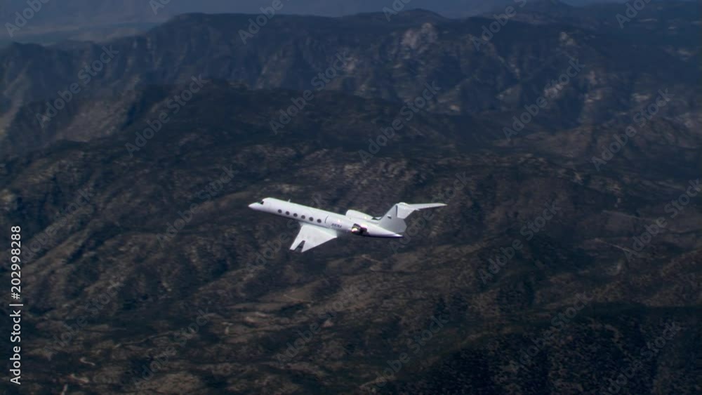 Air-to-air side view of executive jet over rugged terrain Air-to-air side view of executive jet over rugged terrain
