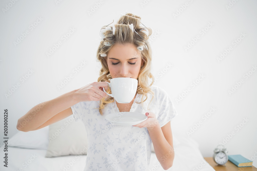 Relaxed pretty blonde wearing hair curlers drinking coffee Relaxed pretty blonde wearing hair curlers drinking coffee