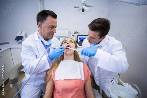 Dentists examining a female patient with tools