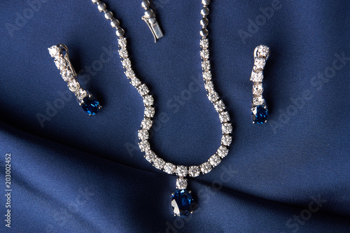 Close-up of women's platinum necklace and earrings with a diamond and blue precious sapphire stone . Luxury female jewelry