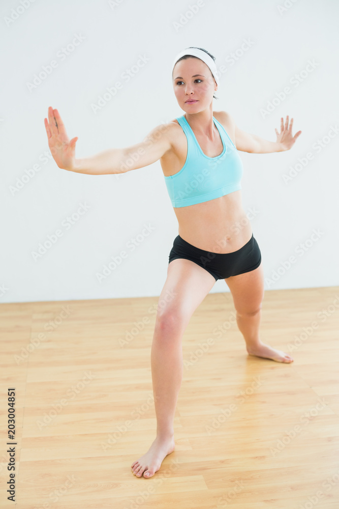 Naklejka premium Toned woman doing the warrior yoga pose in fitness studio