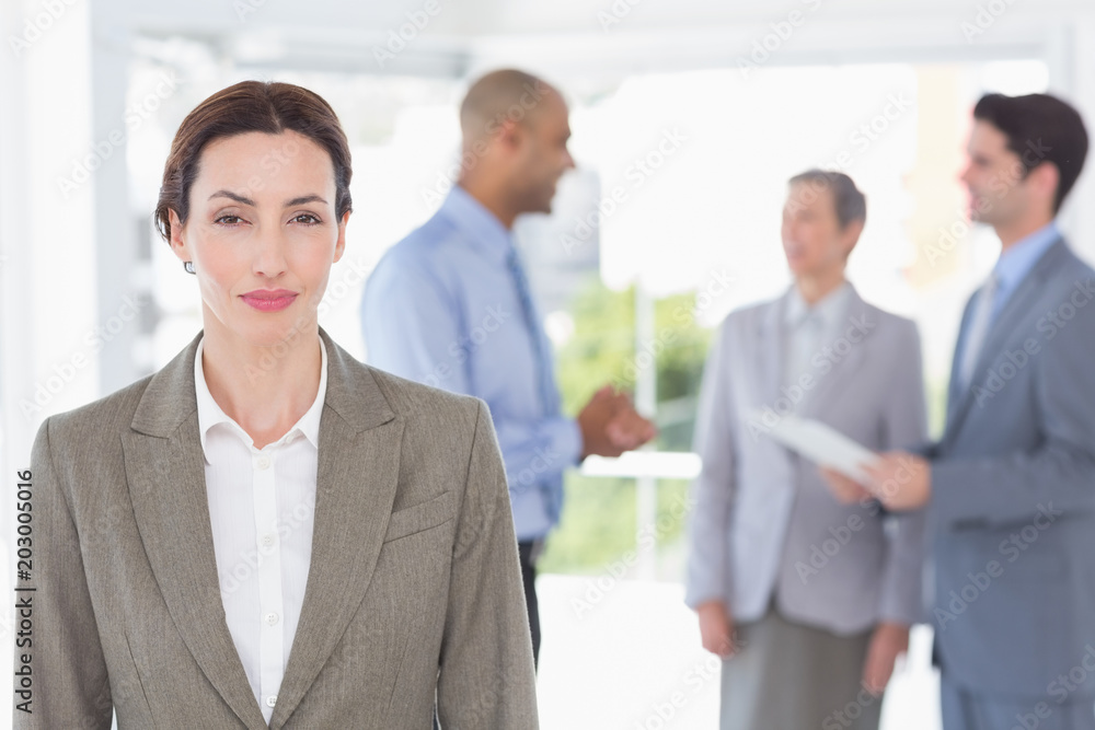 Businesswoman smiling at camera while her colleagues discussing 