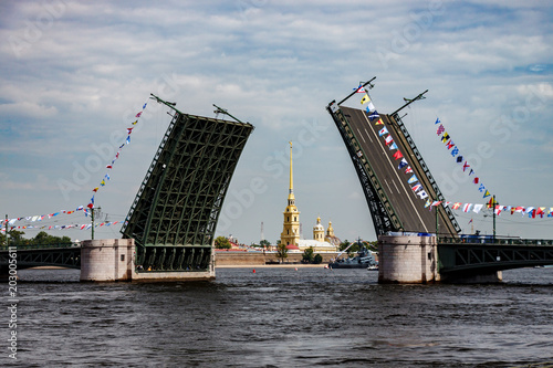 A diluted palace bridge decorated with flags on the Neva River in the city of St. Petersburg. Between the diverged spans of the bridge is seen Peter and Paul Cathedral and the fortress.  photo