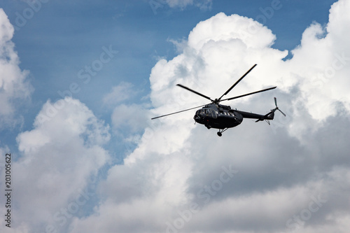 Black military transport helicopter on a background of white clouds and blue sky. MI-8